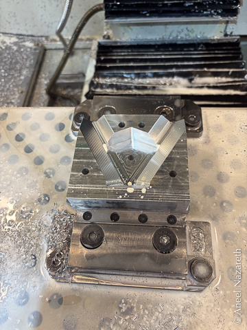 A block of aluminum in the vise of a CNC mill with a V-groove cut in it